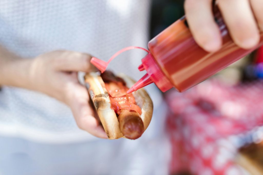 Person putting ketchup on hot dog